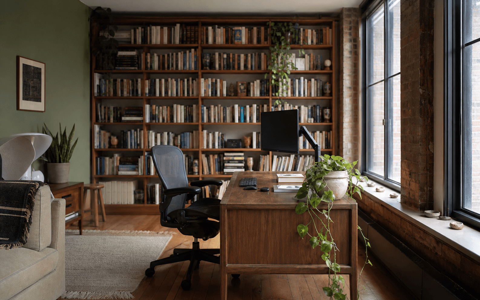 Brooklyn writer's loft home office — walnut desk, brick wall, sage paint, books